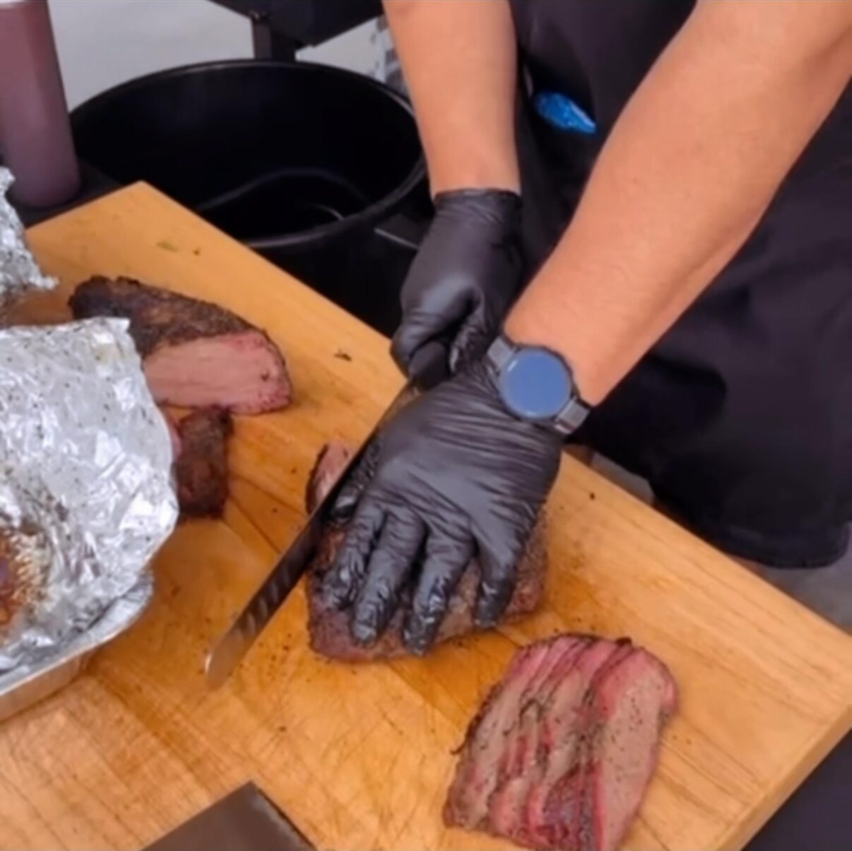 Gloved hands slicing tri-tip on the board